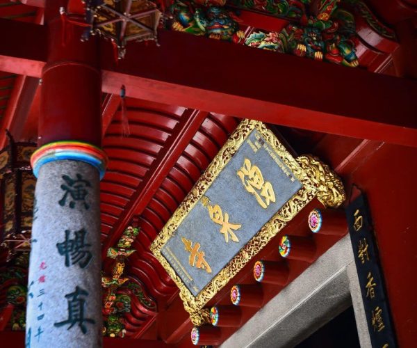 Yongquan Temple,Fuzhou,Chinatravel Ornate Chinese temple interior with a gold-framed plaque and red pillars, colorful carvings above and hanging lanterns nearby.