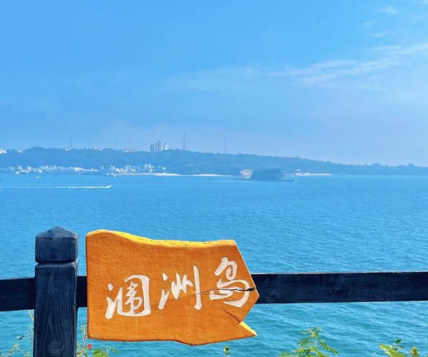 Weizhou Island,Beihai,Chiantravel Weizhou Island,Beihai,Chinatravel Coastal scene with a dark wooden railing, an orange sign with white Chinese characters, and blue ocean beyond.