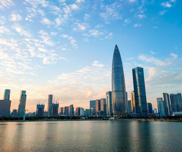 Shenzhen Weathe,Shenzhen,Chinatravel City skyline along a calm river at sunset, with a tall glass skyscraper and other modern buildings reflected in the water