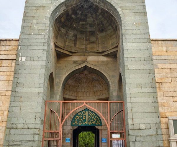 Qingjing Mosque,Quanzhou,Chinatravel Stone fortress gate with a tall arched entrance and a green-tresco archway over the door, flanked by brick walls.