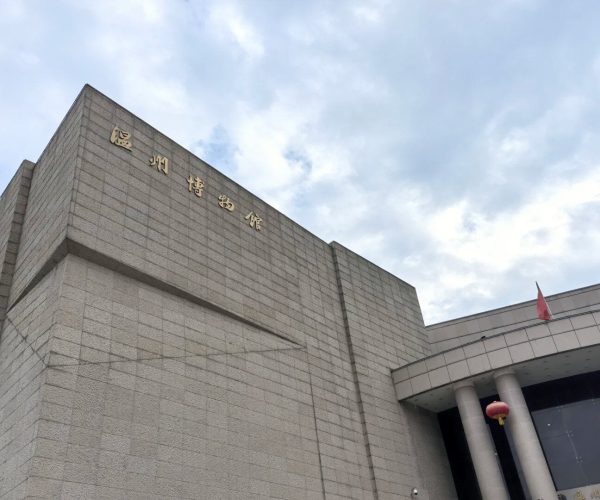 Wenzhou Museum,Wenzhou,Chinatravel Grey stone museum building with gold Chinese characters on the upper facade, a curved entrance, and a red lantern hanging near the door