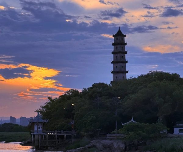 Jiangxin Island,Wenzhou,Chinatravel Silhouette of a multi-tier pagoda on a hill by a calm river at sunset, with orange and purple clouds in the sky and trees around.