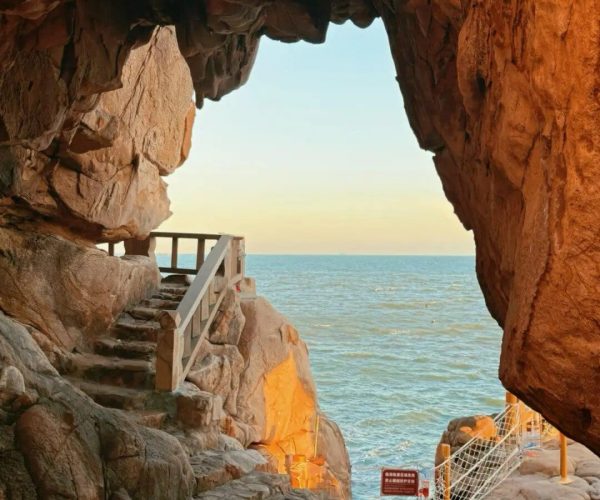 Meizhou Island Scenic Area,Putian,Chinatravel Rocky coastal cave opening with a wooden handrail and stairs leading to the sea at sunset.