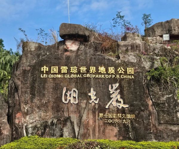 Lakeside Rock,Zhanjiang,Chinatravel Rock sign with gold lettering reading 'LEI QIONG GLOBAL GEOPARK OF P.R. CHINA' (Chinese characters above), set in front of trimmed bushes under a blue sky.