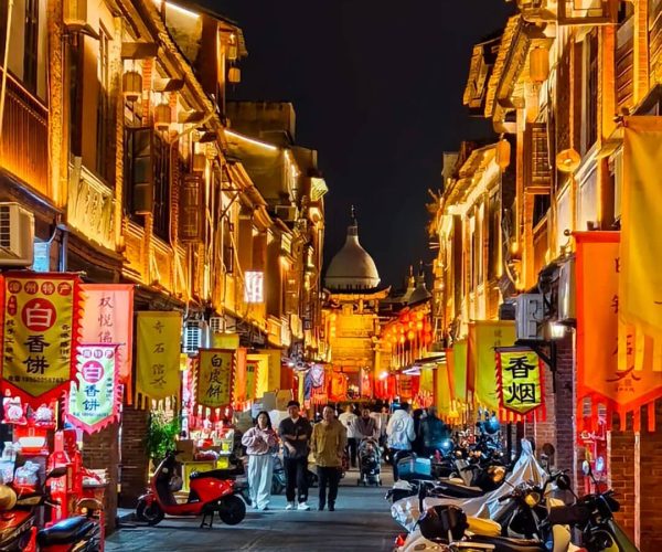 Zhangzhou Ancient City,Zhangzhou,Chinatravel Night market street at night with warm lanterns, colorful banners, and scooters parked along the curb; people stroll under glowing lights.