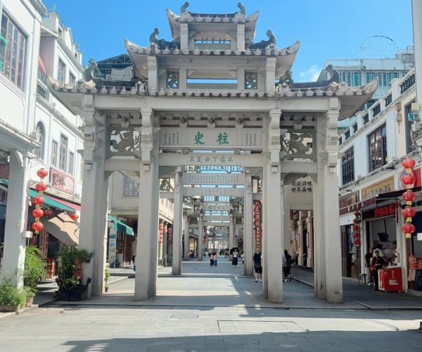 Paifang Street,Chaozhou,Chinatravel Multi-tiered Chinese paifang gate spans a pedestrian shopping street with shops on both sides and red lanterns under a bright blue sky.