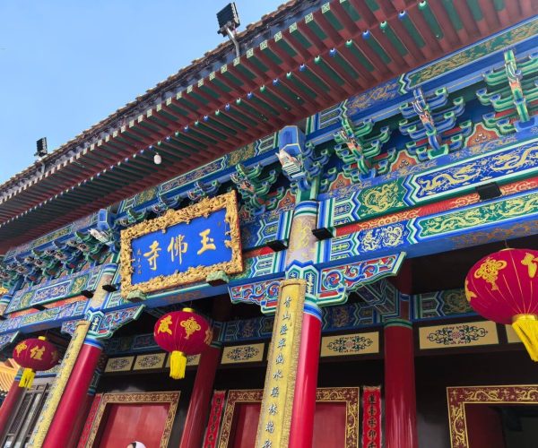 Jade Buddha Garden,Anshan,China tour Ornate Chinese temple entrance with blue and gold plaque, colorful beams, and red lanterns hanging between red columns.