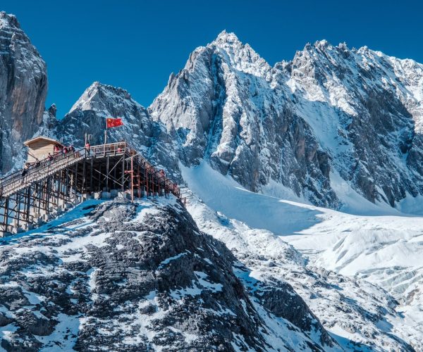 Yulong snow Mountain,Lijiang,Chinatravel Wooden viewing platform on a snowy rocky ridge with a red flag, set against towering snowy mountains.
