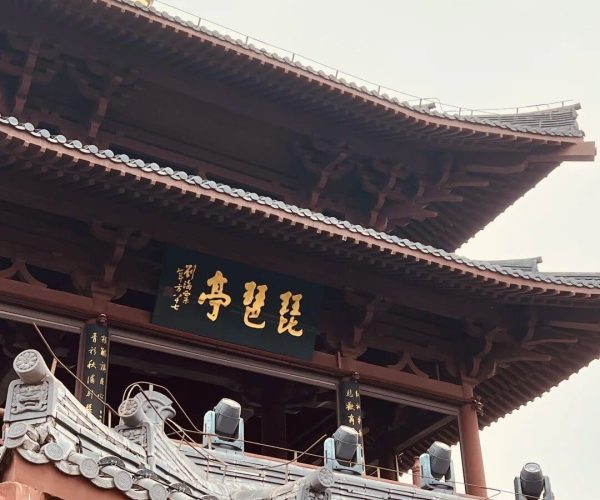 Pipa Pavilion,Jiujiang,China tour Traditional Asian temple roof with dark wooden beams, curved gray tiled eaves, and a black plaque with gold Chinese characters.