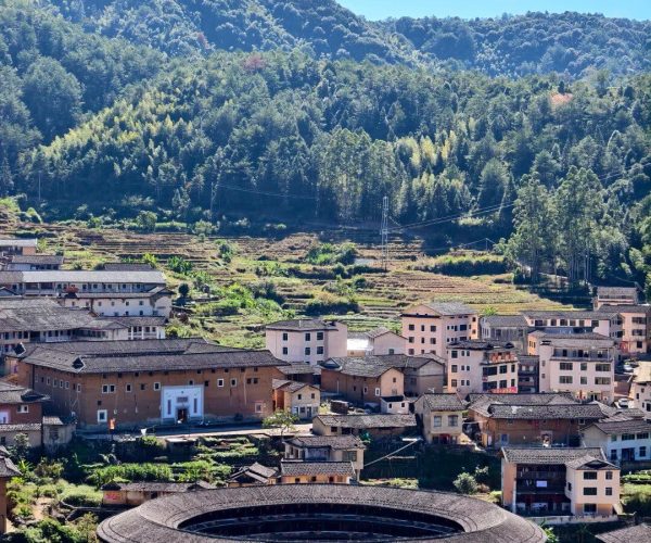 Tianluokeng Tulou Cluster,Zhangzhou,Chinatravel Circular tulou earth buildings clustered in a valley village, with terraced fields and forested hills under a blue sky.