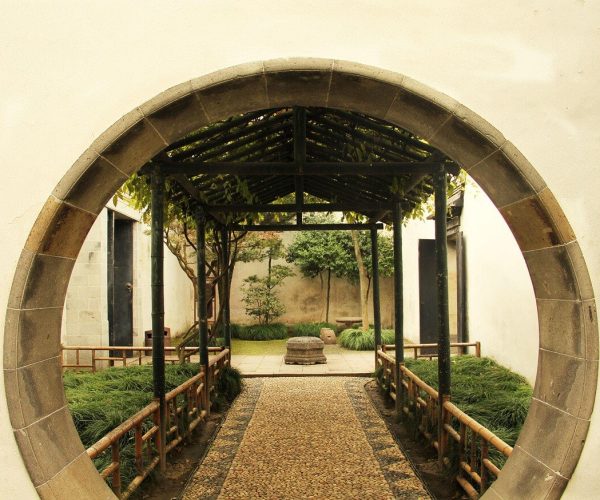 Lingering Garden,Suzhou,Chinatravel Circular stone gate framing a stone path through a tranquil garden courtyard with greenery on both sides.
