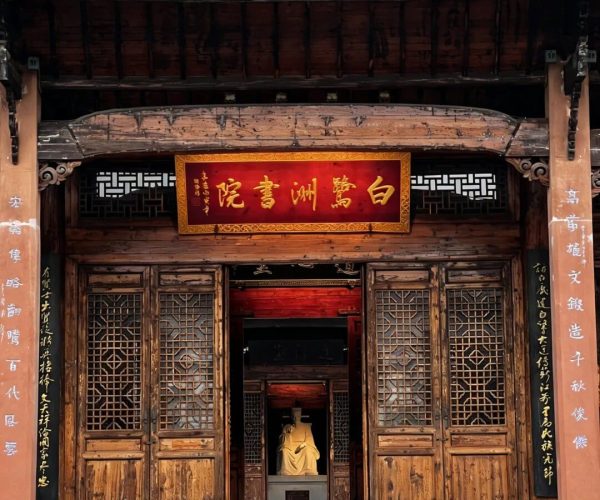 Bailuzhou Academy,Ji'an,China tour Entrance to a traditional Chinese temple with weathered wooden doors and a red-gold sign above the doorway, visible statue inside.