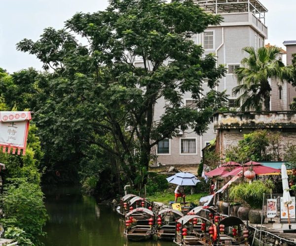 Foshan Ancient Water Towns,Foshan,Chinatravel Waterway with wooden boats docked along a canal next to a market, green trees, and a gray building in the background.