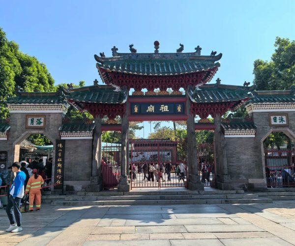 Ancestral Temple,Foshan,Chinatravel Ornate Chinese temple gate with green tiled roof and red decorative beams; people enter a courtyard beyond iron gates.