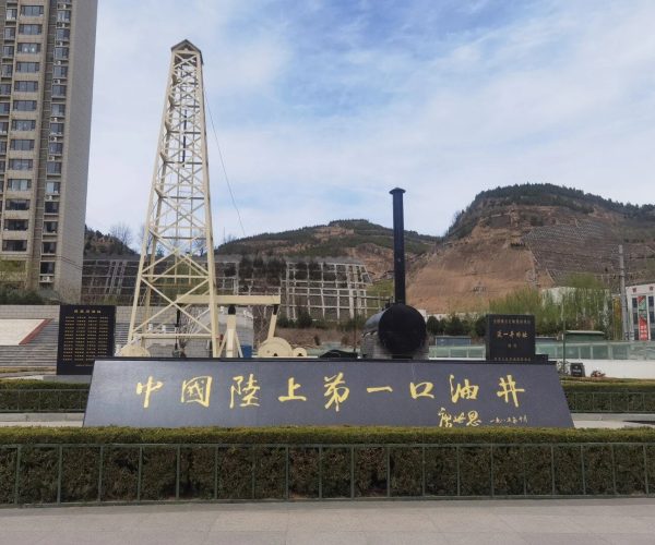 Daqing Oil Well №1 Site,Daqing,Chinatravel Outdoor monument with a large dark plaque bearing gold Chinese characters, set in front of an oil drilling rig and hillside backdrop.
