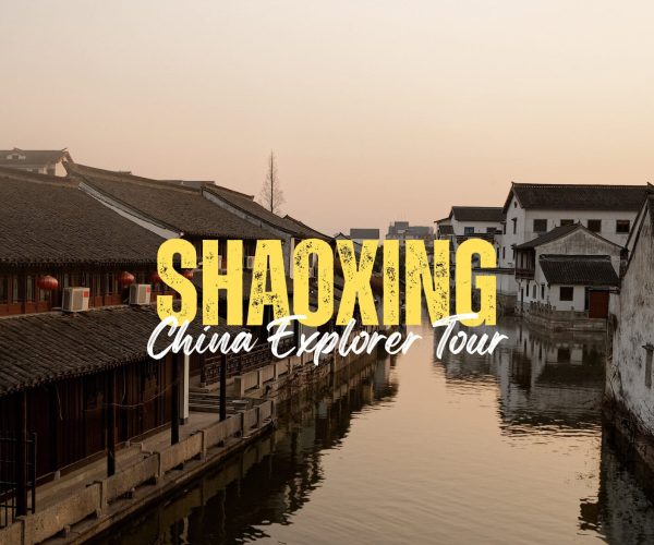 Shaoxing,Zhejiang,Chinatravel Promotional banner for a Shaoxing China Explorer Tour with bold yellow 'SHAOXING' text over a canal-side town at sunset, with a cursive 'China Explorer Tour' subtitle is visible over the water.
