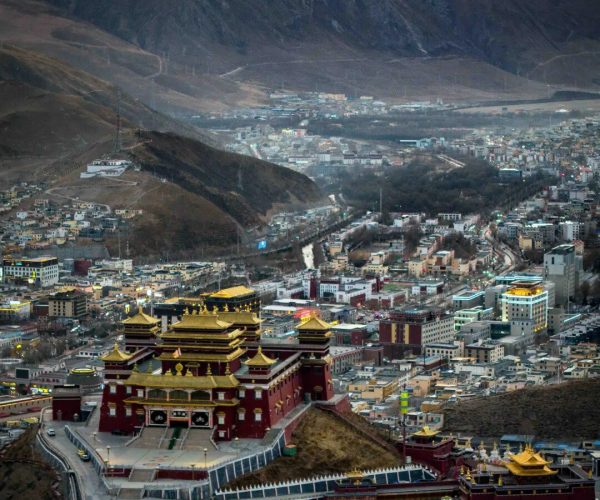 Jyeku Monastery,Yushu,China tour A Buddhist monastery complex with gold-roofed pagodas atop a hill, overlooking a city in a valley with dark mountains in the distance.