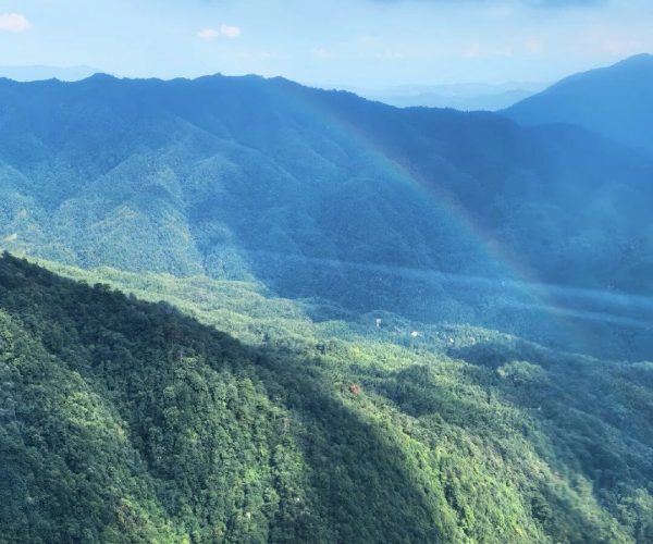 Yangshimu,Ji'an,China tour Panoramic view of green forested mountains under a blue sky with a faint rainbow.