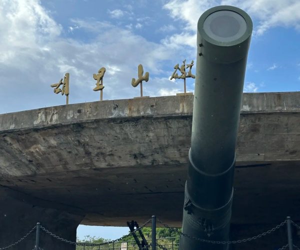 Hulishan Fortress,Xiamen,Chinatravel Large dark artillery gun mounted on a concrete pedestal, barrel angled upward, with Chinese characters along the edge and chain barriers in front.