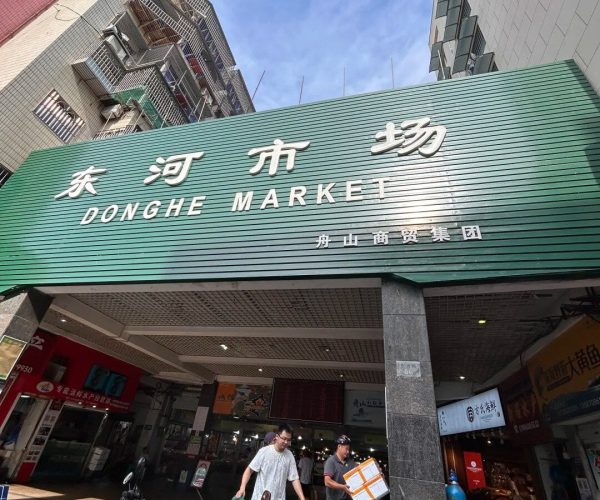 Donghe Seafood Market,Zhoushan,Chinatravel Entrance sign of Donghe Market on a green facade, with shoppers and delivery people unloading outside the market.