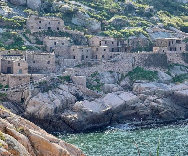 Dongji Island,Zhoushan,Chinatravel Stone houses perched on steep rocky cliffs above a calm, blue-green sea.
