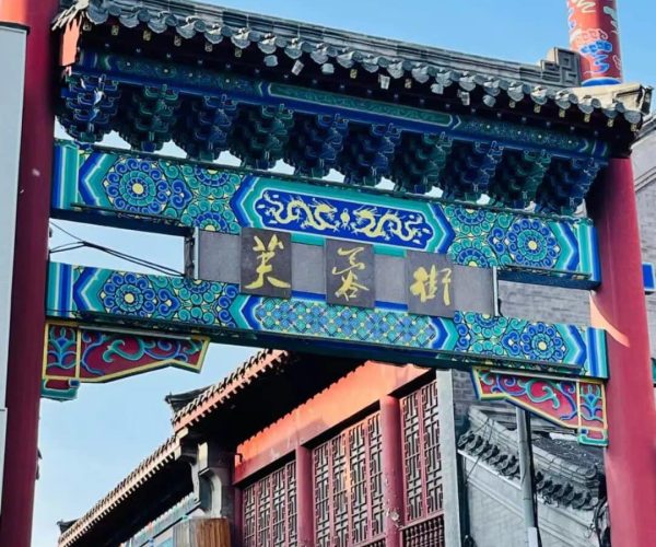 Furong Ancient Street,Jinan,China tour Ornate Chinese archway with blue-green patterns and gold characters, flanked by red columns, opening to a street with shops.