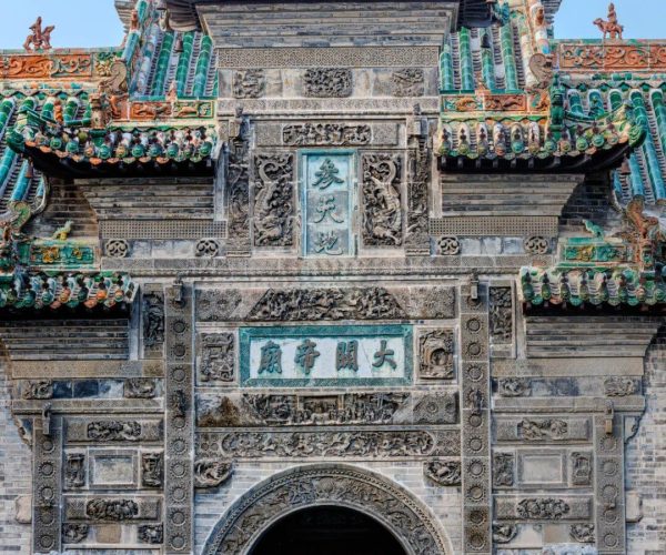Huaxi Towe,Bozhou,China tour Ornate Chinese temple gate with green glazed tiles, stone carvings, and dragon statues flanking an arched entrance.