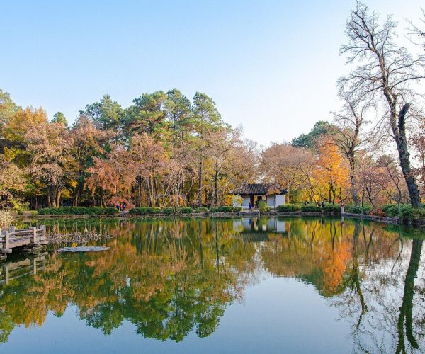 Suzhou Weather,Suzhou,Chinatravel Autumn park scene with a calm pond, colorful trees, and a small pavilion reflected in the water. a wooden walkway extends over the pond on the left.