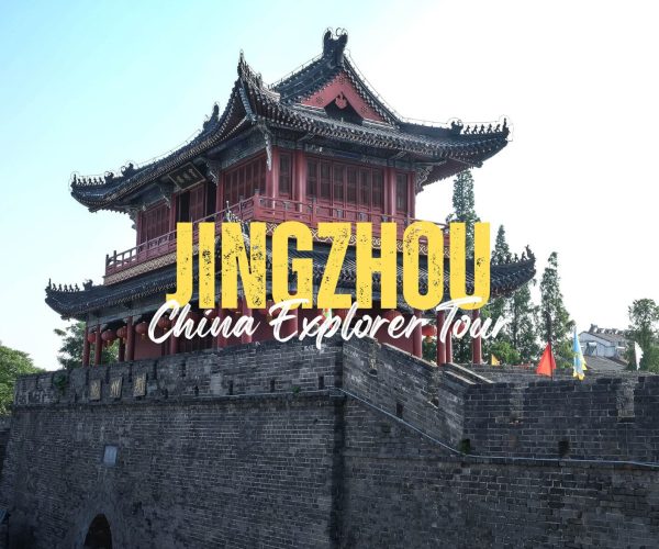 Jingzhou,Hubei,Chinatravel Historic Chinese tower perched on a stone city wall, with large yellow text 'JINGZHOU' and cursive 'China Explorer Tour' overlay against a blue sky.