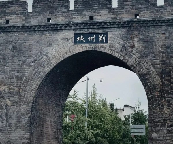 Jingzhou Ancient City Wall,Jingzhou,Chinatravel Ancient stone archway with battlements and a Chinese plaque above the arch, opening onto a tree-lined street.