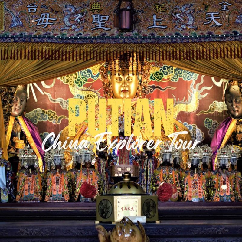 Putian,Fujian,Chinatravel Golden Buddha statue in a richly decorated shrine, flanked by smaller elaborately dressed figures and ceremonial objects, with bold yellow overlay text reading 'Pilan China Explorer Tour' across the front.