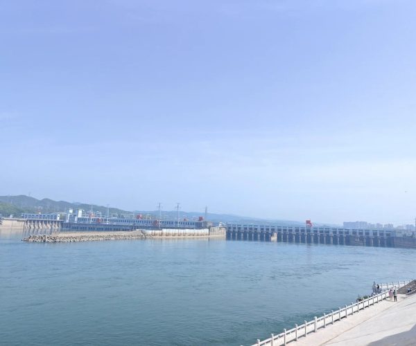 Gezhouba Water Conservancy,Yichang,Chinatravel Wide river with a long concrete dam or bridge spanning the water, and a waterfront walkway on the right where a few people stroll under a clear blue sky