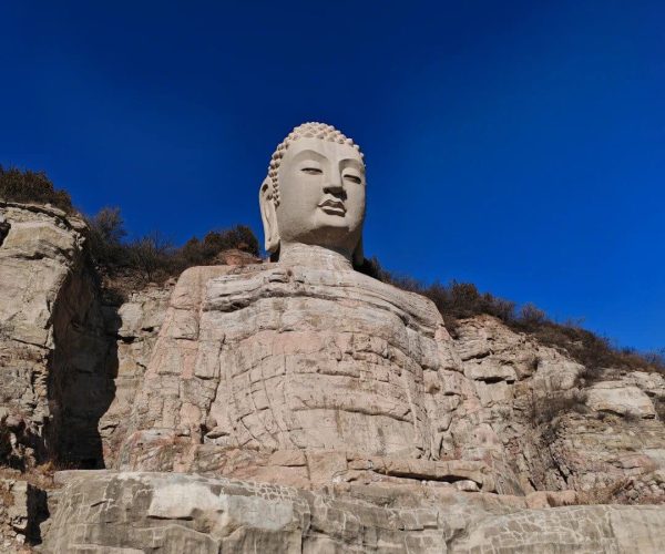 Mengshan Giant Buddha,Taiyuan,Chinatravel Colossal stone Buddha carved into a rocky hillside beneath a clear blue sky, with small Buddha figures in rock alcoves at the base.