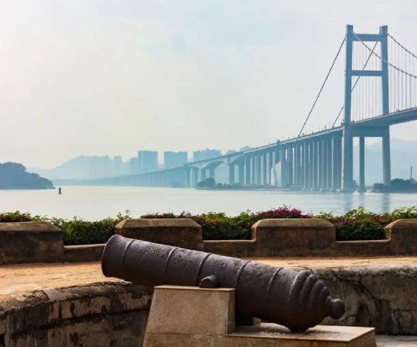 Humen Fort,Dongguan,Chinatravel Old cannon on a stone platform overlooking a calm harbor with a long suspension bridge in the distance