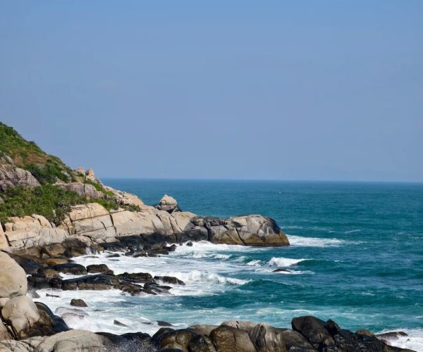 Wuzhizhou Island,Sanya,Chinatravel Rocky coastline with waves crashing against smooth granite boulders under a clear blue sky on a sunny day.
