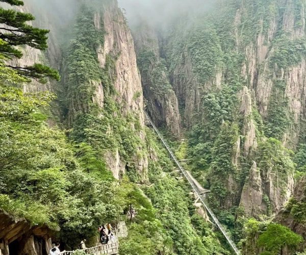 Xihai Grand Canyon,Huangshan,Chinatravel Suspension bridge along a steep, forested canyon with mist and hikers on a wooden walkway.