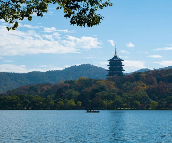 West Lake,Hangzhou,Chinatravel Pagoda on a hill by a calm lake with autumn trees and a small boat on the water under a blue sky.