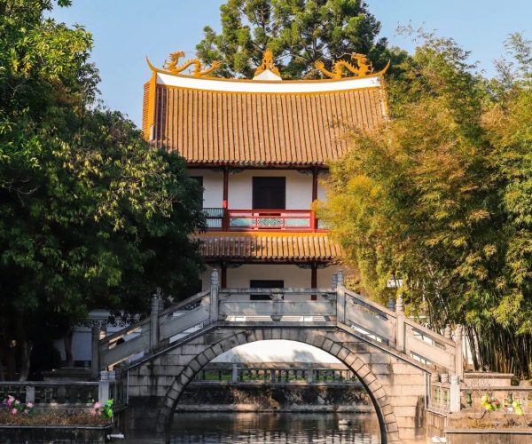 Xichan Temple,Fuzhou,Chinatravel Traditional Chinese temple with orange tile roof and dragon ornaments, seen behind a stone arch bridge over a tranquil pond.