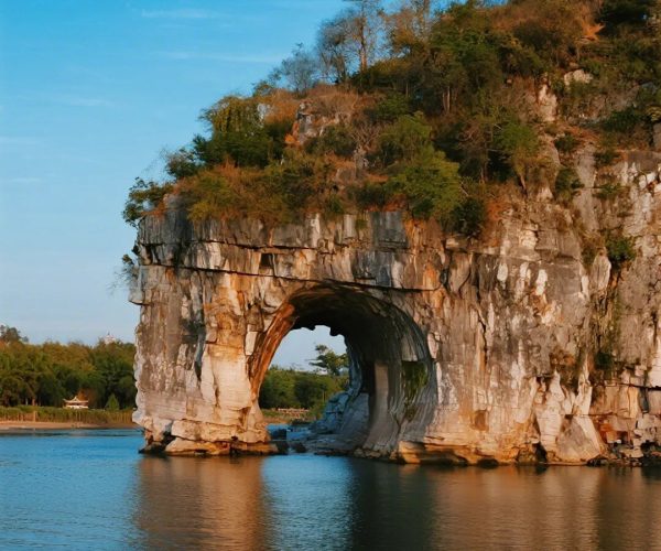 Elephant Trunk Hill,Guilin,Chinatravel Natural rock arch rising from calm water with a tree-covered cliff above under a clear blue sky