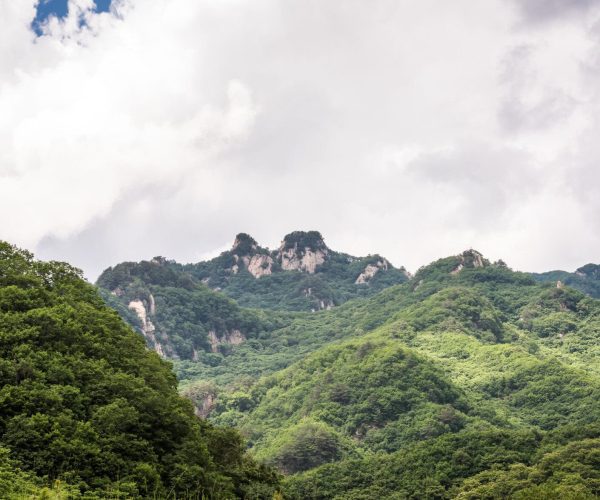 Liaoning Weather,Liaoning,China tour Lush green forested hills with rocky mountain peaks under a cloudy sky