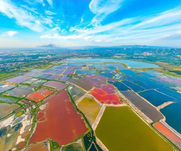 Yuncheng Salt Lake,Yuncheng,Chinatravel Aerial view of colorful salt evaporation ponds in a patchwork of reds, greens, and blues next to a blue sky and distant hills.