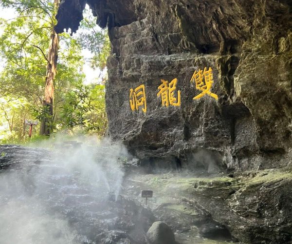 Jinhua Shuanglong Cave,Zhejiang,Chinatravel Rock cave wall with four bright gold Chinese characters carved into the stone, mist rising from a damp path below and trees visible in the background.