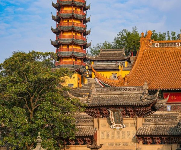 Jinshan Temple,Zhenjiang,China tour Five-story yellow pagoda with curved green-tiled roofs in a Chinese temple complex against a blue sky, with surrounding orange-roofed buildings.