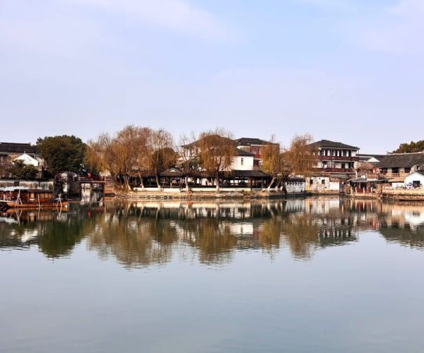 Jinxi Ancient Town,Kunshan,China tour Calm lake reflecting traditional Chinese buildings and leafless trees along a riverside town against a blue sky