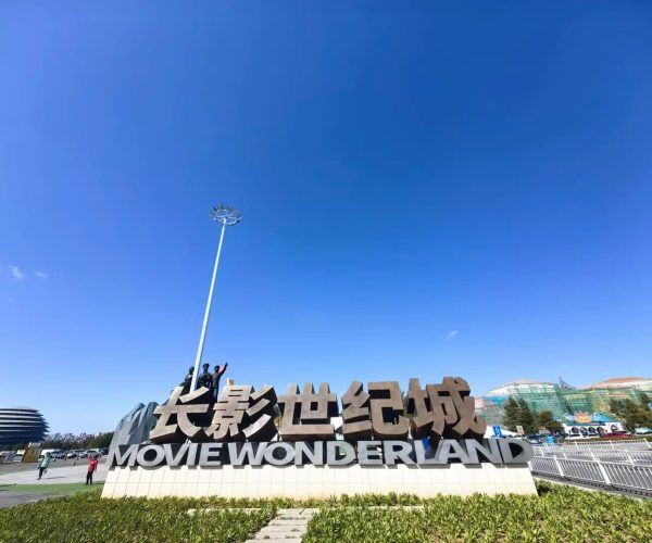Changchun Movie Wonderland,Changchun,China tour Giant sign reading 'Movie Wonderland' in English and Chinese, with visitors posing beneath a tall streetlamp against a bright blue sky.