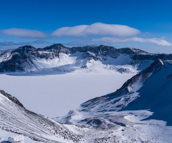 Changbai Mountain,Baishan,Chinatrip Snow-covered mountain crater with jagged ridges under a clear blue sky and a lenticular cloud overhead.
