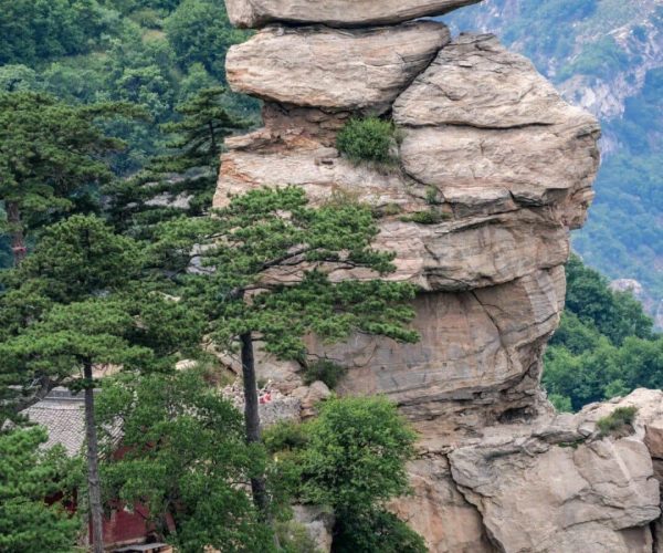 Fuping Temple,Baoding,China tour Tall stacked rock formation with three large boulders balanced on each other, surrounded by green trees and a distant mountain range in the background.
