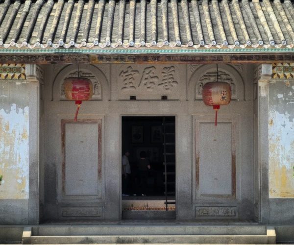 Chen Cihong's Former Residence ,Shantou,Chinatravel Stone temple facade with ornate carvings, a tiled roof, and red lanterns hanging at the doorway; open entrance reveals visitors inside.