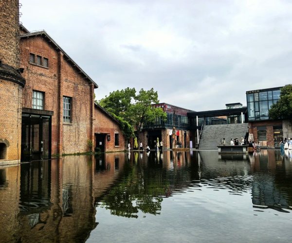 Jingdezhen Ceramic Cultural Park,Jingdezhen,China tour Brick factory buildings surround a large reflecting pool with people strolling along the water’s edge and a modern glass building in the background.
