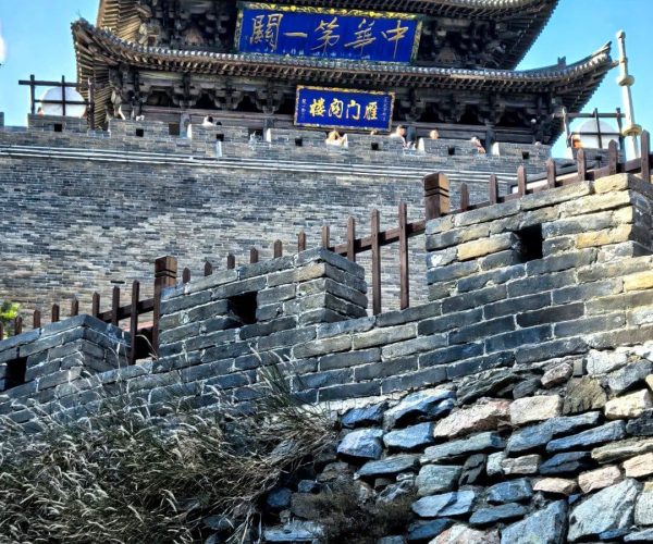 Yanmen Pass,Xinzhou,Chinatravel Traditional Chinese gate atop a stone fortress wall under a bright blue sky, with blue plaque signs.